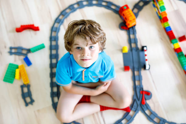 istock Adorable little blond kid boy playing with colorful plastic blocks and creating train station. Child having fun with building railway toys at home 1210960265