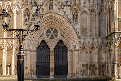 York, UK. March 4, 2020. The central West facing wooden doors of York Minster set in an ornate archivolt. Twin lamps are in the foreground.