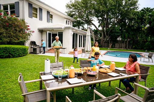Multi-generation Hispanic family gathering at a backyard table for a summertime cookout in Miami, Florida.