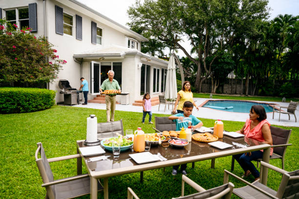 Latin American family gathering at table for outdoor meal Multi-generation Hispanic family gathering at a backyard table for a summertime cookout in Miami, Florida. back yard stock pictures, royalty-free photos & images
