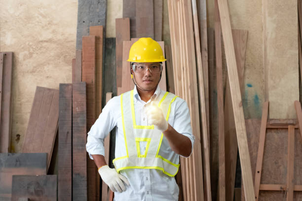 istock Handsome man wearing protective glasses and yellow helmet,raise blurred left hands up with determind eyes,standing in front of wood pile,at factory 1210971978