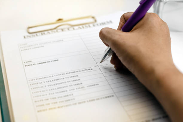 istock Pen was holding by human hand,writing on Insurance claim form,blurry light around 1210971980