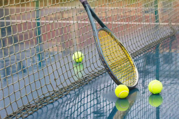 Racket and wet tennis balls on court covered with rain stock photo