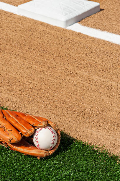 une balle de baseball dans un gant le long de la ligne de base du champ intérieur d’un diamant de base-ball - baseball diamond baseball baseline grass photos et images de collection