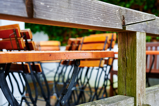 Looking through a wooden terrace railing to tables and folded chairs of a restaurant in bad weather.