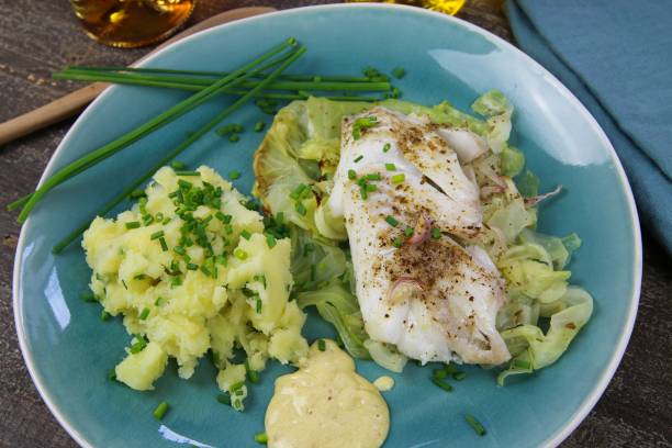 istock Isolated blue china dish with codfish fillet poached on pointed cabbage, mustard sauce and mashed potatoes seasoned with chives 1210980144