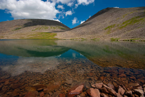 Tranquil autumn landscape with clouds reflection on smooth mirror surface of mountain lake in high hanging valley. Meditative view from calm alpine lake to mountain vastness. Stones in clear water.