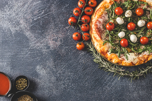 Delicious pizza, fresh cherry tomatoes, rosemary and spices on dark background
