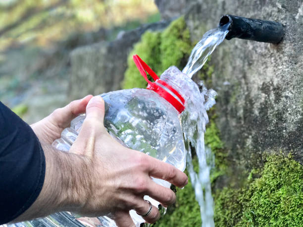 istock Man`s hand holding plastic water bottle  and collect fresh water from spring. 1210994671