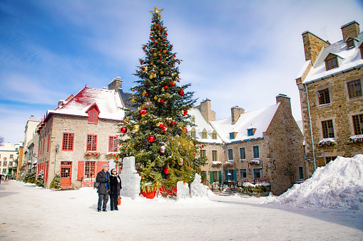 Senior couple enjoying the Place Royale in old Quebec City on a Winter day, next to the imposing Christmas tree.