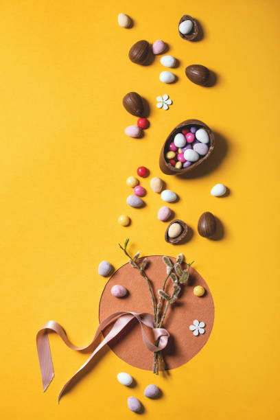 Easter greeting card Easter greeting card with blossom willow branches, chocolate sweets and eggs on bright orange yellow background. Flat lay, copy space. bud candy stock pictures, royalty-free photos & images
