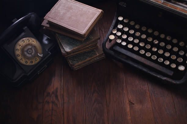 Old retro phone with vintage typewriter and books on wooden table