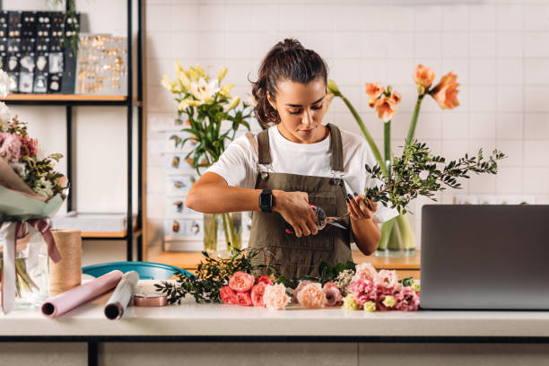 kobieta kwiaciarnia cięcia łodyg w kwiaciarni stojąc przy kasie - florist zdjęcia i obrazy z banku zdjęć
