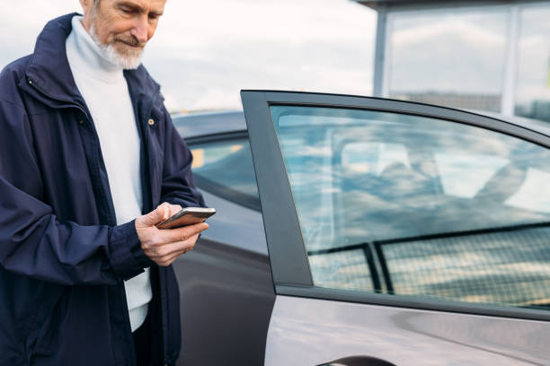 istock Senior man typing on cell phone while standing at rental car 1211010053