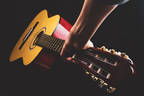 istock Hand holds guitar. acoustic musical instrument on black background 1211012303