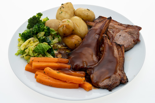 Grilled lamb chops dinner with steamed vegetables, new potatoes and gravy - white background