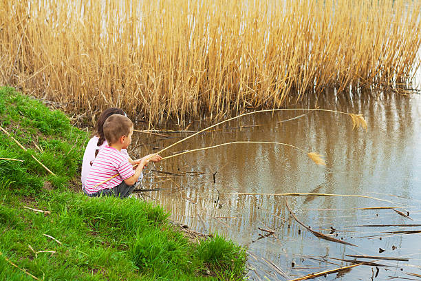 Young siblings discussing how to build a dam with rock at river side with a Canadian forest in the background.