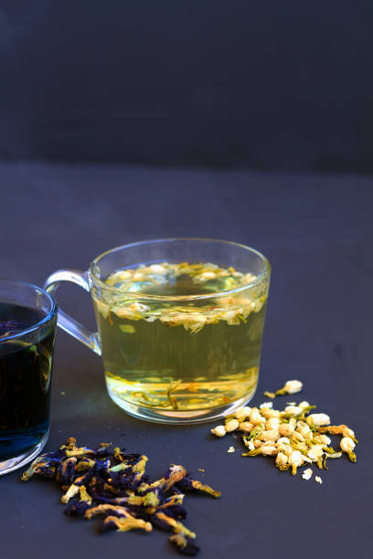 tè al gelsomino. bevande calde. stile di vita sano. tazza di vetro di tè al gelsomino su sfondo nero. tazza di tisana calda con fiori secchi di gelsomino su un tavolo nero. spazio di copia. orientamento verticale - tea jasmine tea green black foto e immagini stock