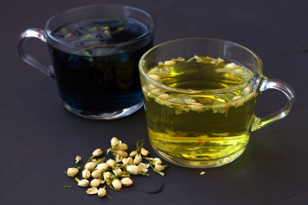 thé aux pois papillons et thé au jasmin. deux tasses de thé chaud avec des fleurs sèches sur une vue noire de dessus de table. sain. tasses en verre de tisane bleue et jaune sur un fond noir. des boissons chaudes. - jasmine tea black tea tea drink photos et images de collection