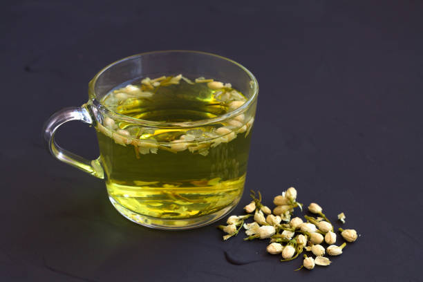 tè al gelsomino. tazza di tisana calda con fiori secchi di gelsomino su un tavolo nero con spazio di copia. bevande calde. stile di vita sano. tazza di vetro di tè al gelsomino su sfondo nero. - tea jasmine tea green black foto e immagini stock