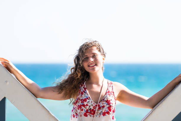 jeune fille heureuse de femme de sourire près de la plage avec l’océan de mer dans le vent soufflant le temps ensoleillé de cheveux et le pavillon - 13414 photos et images de collection