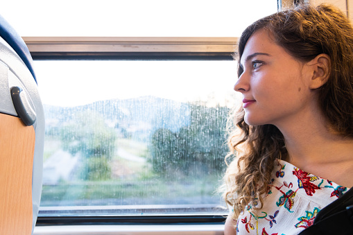 Woman young girl tourist sitting inside train in Italy with modern on seat side profile portrait closeup with view of Tuscany