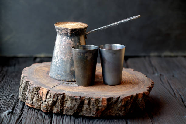 Vintage shiny copper turkish coffee pot and cups at dark oak table, black background