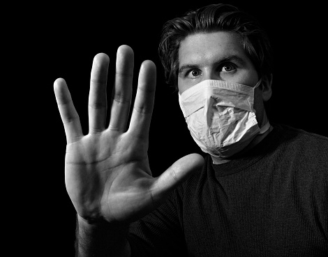 a masked man gesturing to stay or way or to avoid getting a virus.