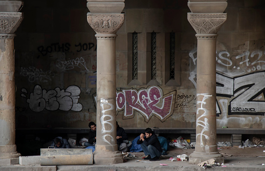 Belgrade, Serbia - October 17, 2019 : Group of young male refugees waking up in a dirty shelter under the city street downtown bridge