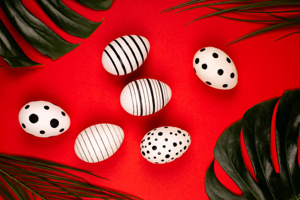 istock Creative graphic eggs with green tropical leaves on bright red background. 1211046332