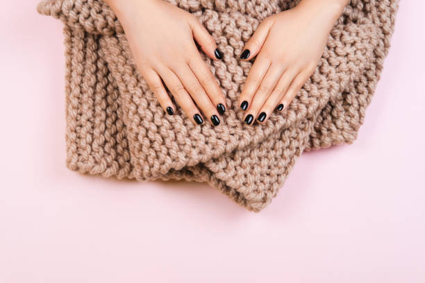 istock Black manicure with cozy wool knitted scarf on pastel background. 1211046351