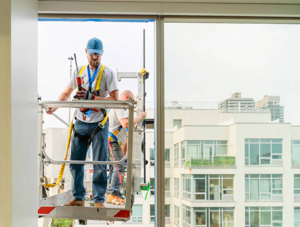 istock Team of blue-collar workers replacing a broken window in the office building - applying a fresh sealant for a new glass installation. High-altitude work on the lifting platform which is placed outside. 1211046969