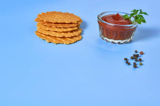 istock Many thin spicy waffles, savory sauce and scattered pepper on purple background. Copy space 1211063050