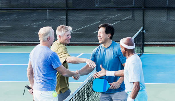Group of senior men shaking hands on pickleball court A multi-ethnic group of four mature and senior men shaking hands and smiling on a pickleball court. The African-American man is the oldest, in his 70s. They are greeting each other, or perhaps congratulating each other after a fun match. paddle ball stock pictures, royalty-free photos & images