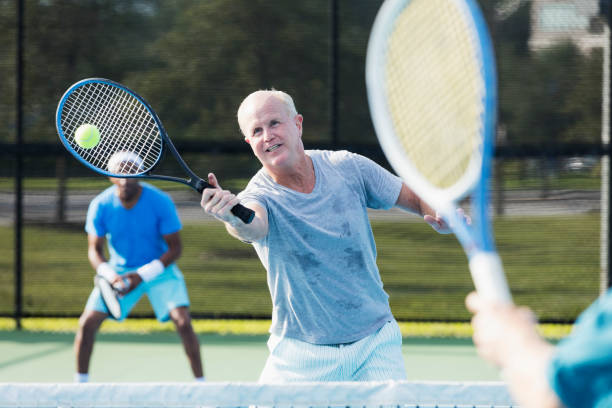 men playing tennis, hitting a volley - tennis active seniors healthy lifestyle senior men imagens e fotografias de stock