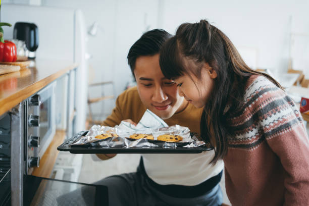 father with daughter baking cookies together in the kitchen and smelling freshly baked cookies straight from the oven - men asia asian culture asian ethnicity imagens e fotografias de stock