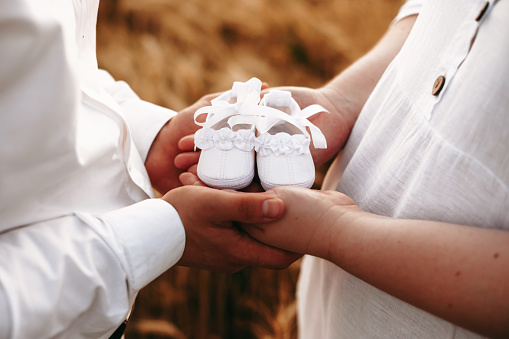 Caucasian plump woman expecting a baby is posing near her lover holding a pair of shoes for kids