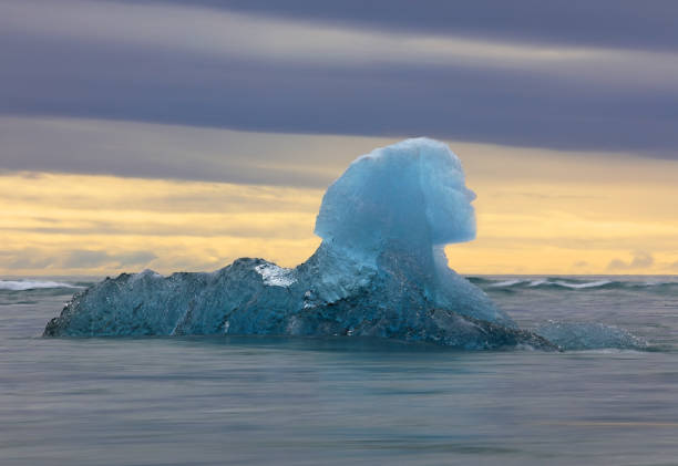 A Sphinx shaped block of ice floats out to sea against a dramatic sunset sky