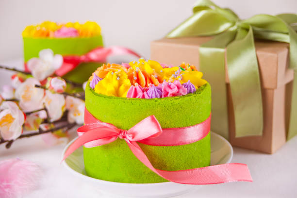 Spring Easter festive table. Small green cake with butter cream flowers, cherry blossom branch and gift box on the background