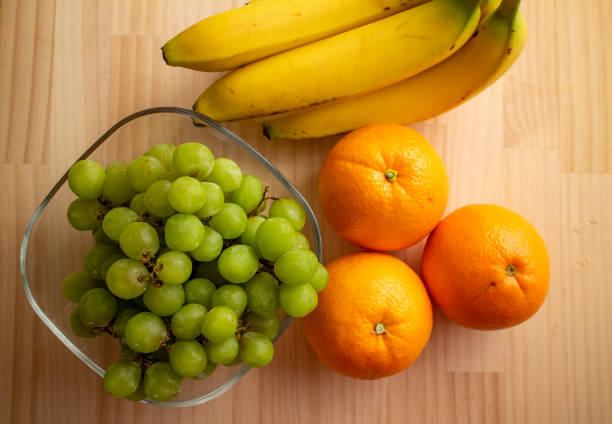 Fresh and delicious raw green grapes, oranges and bananas on a natural wooden table.