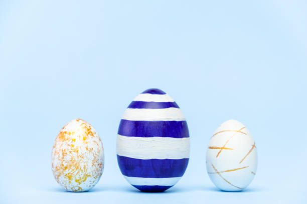 istock Three easter trendy colored classic blue and golden decorated eggs on blue background. Happy Easter card with copy space for text Minimal easter style 1211094803