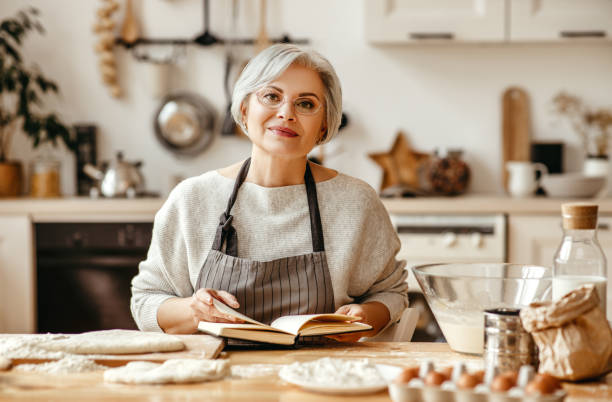 счастливая старуха бабушка повара на кухне месит тесто, печет печенье - grandmother domestic life cooking domestic kitchen стоковые фото и изображения