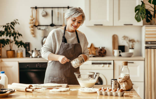 счастливая старуха бабушка повара на кухне месит тесто, печет печенье - grandmother domestic life cooking domestic kitchen стоковые фото и изображения