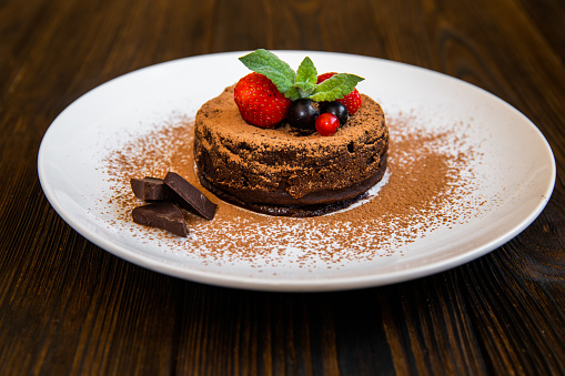 Chocolate fondant lava cake decorated with strawberries and cocoa powder on a wooden background
