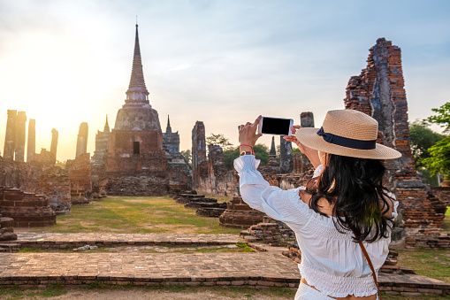 Tourist woman taking a picture with a mobile phone in touristic ruins of Ayutthaya in Thailand