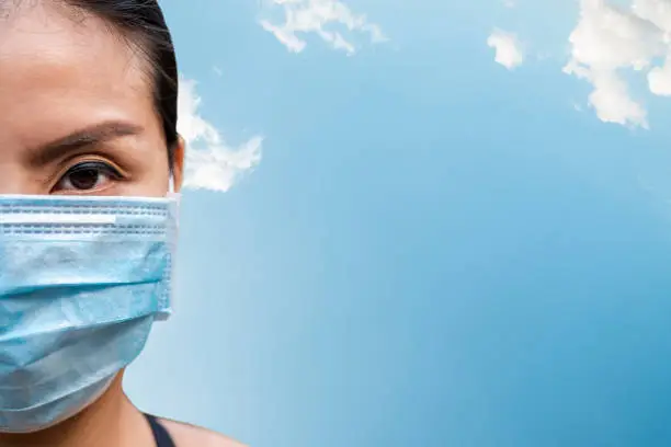 Asian woman wearing a mask against diseases and pollution with copy space in blue sky