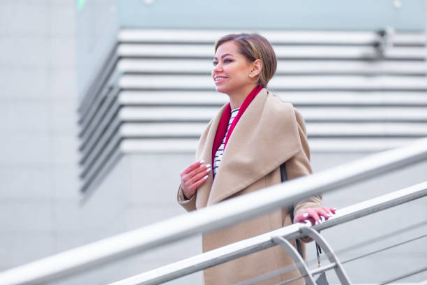 at the mall lifestyle fashion portrait of stunning brunette girl. walking on at the mall. going shopping. wearing stylish white fitted coat, red neckscarf. business woman. black bag - neckscarf imagens e fotografias de stock