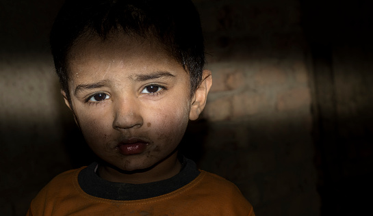 a refugee homeless child standing in a dark room with sad expression