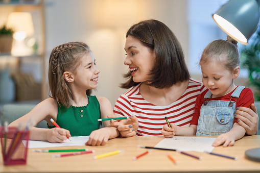 Happy family. Mother and daughters drawing together. Adult woman helping to child girl.