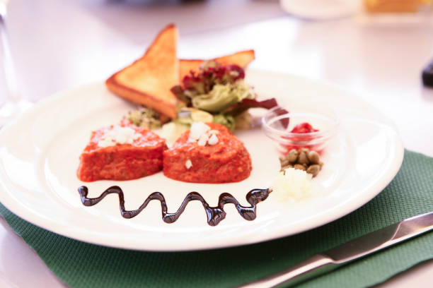 Two pieces of raw meat with toppings on plate in restaurant with fancy decoration